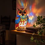 Lámpara búho de vitral encendida sobre un estante de roble por la noche