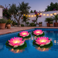 Cuatro lamparas solares flotantes de loto rosa encendidas en una piscina espanola al anochecer